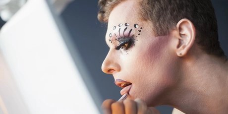 Drag queen doing make up in front of a mirror