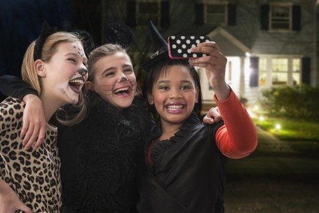 Girls in costumes taking selfie with cell phone on Halloween