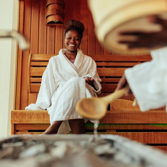 Eine junge Frau sitzt in der Estrel Berlin Sauna, jemand macht einen Aufguß